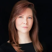 Headshot of a woman with shoulder-length reddish-brown hair against a black background.