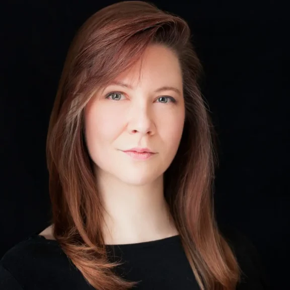 Headshot of a woman with shoulder-length reddish-brown hair against a black background.