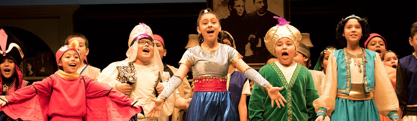 Students dressed in brightly colored costumes performing the musical Aladdin on stage.