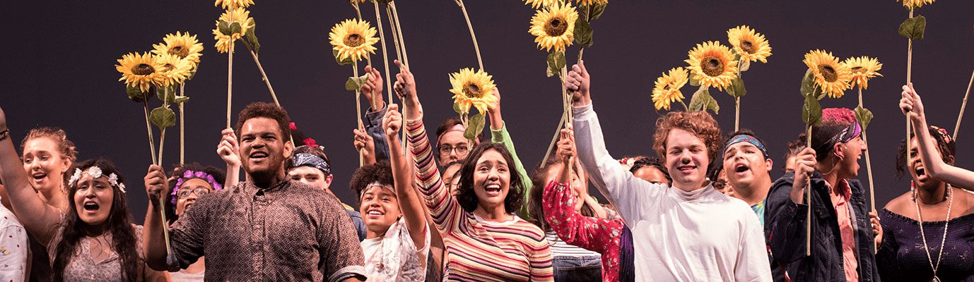 cast members singing and holding sunflowers above their heads