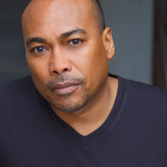 Headshot of a man with a goatee wearing a black v-neck shirt.