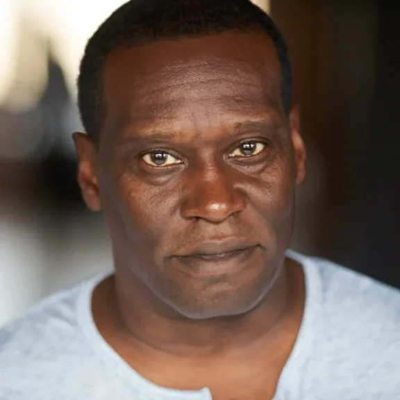 A man with short hair wearing a light gray shirt looks directly at the camera with a neutral expression.