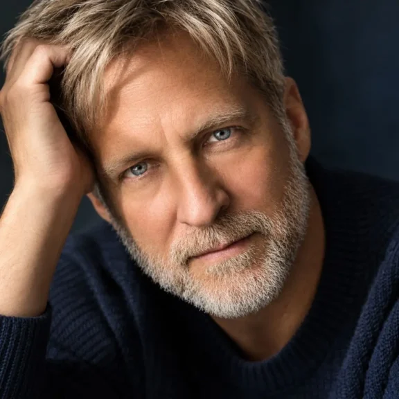 Portrait of a middle-aged man with blue eyes and a salt-and-pepper beard, resting his hand on his head.