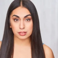 A woman with long straight dark hair and natural makeup looks directly at the camera against a plain light background.
