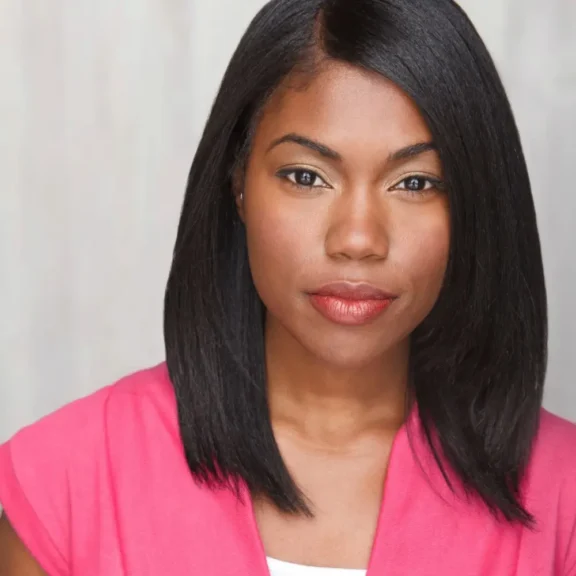 A woman with straight, shoulder-length black hair and a pink top looks directly at the camera against a neutral background.