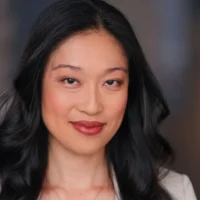 A woman with long black hair and light makeup is looking at the camera with a neutral expression.