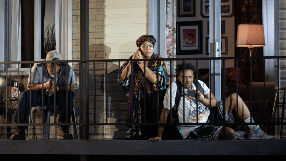 Three people sitting on a porch looking surprised while one is on the phone and another is recording an incident on the street.