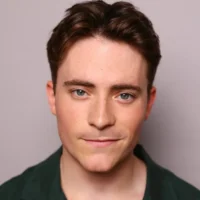 A young man with short brown hair and blue eyes looks directly at the camera, wearing a dark green shirt against a plain light background.