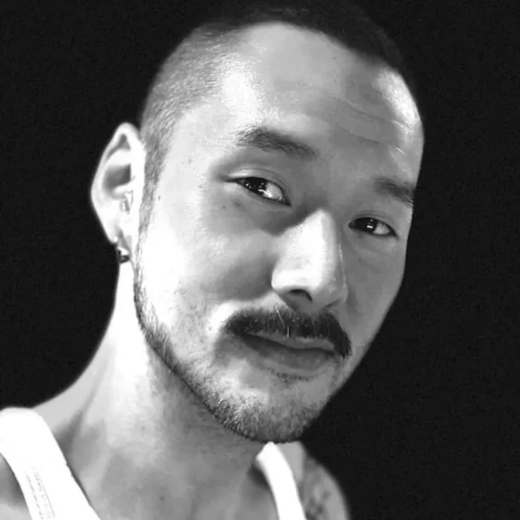 A black-and-white portrait of a man with a mustache, short hair, and an earring.