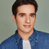 Headshot of a man with dark hair wearing a denim shirt over a white undershirt.