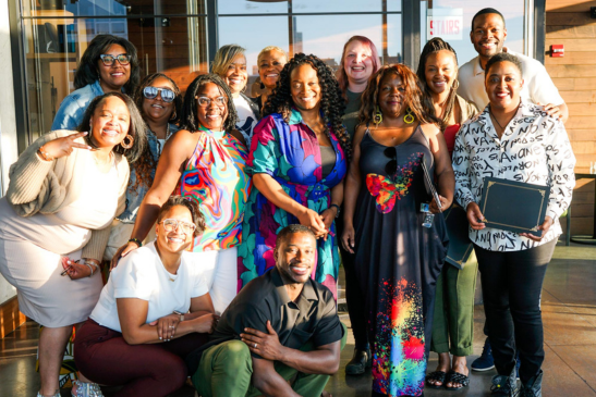 A group of people in formal dress smiling in the sunlight.