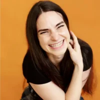 A smiling woman with long dark hair poses against an orange background.