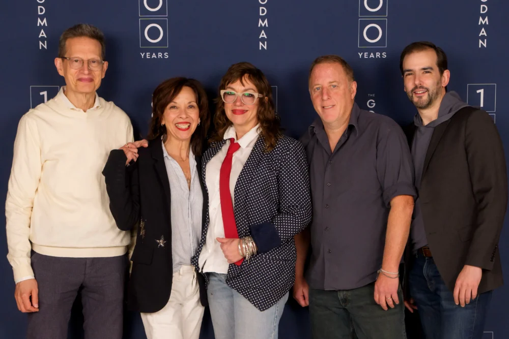 Five people stand together in front of a dark blue backdrop with "Goodman" and "100 Years" logos, posing for a group photo.