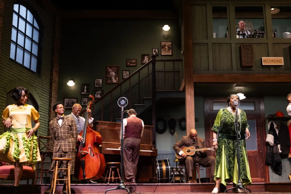 A jazz band performs on stage with various instruments while a woman sings and another woman dances; a recording booth is visible on the upper level.