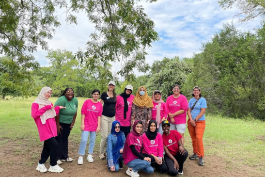 A group of smiling girls and young women posing in a park. Many of them are wearing pink Camp GirlForward shirts.