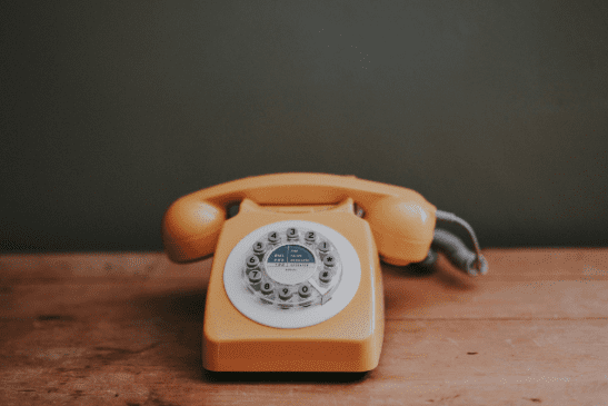 Yellow landline telephone sitting on a wooden desk.