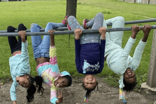 Four laughing children hanging upside down from a playground monkey bar.