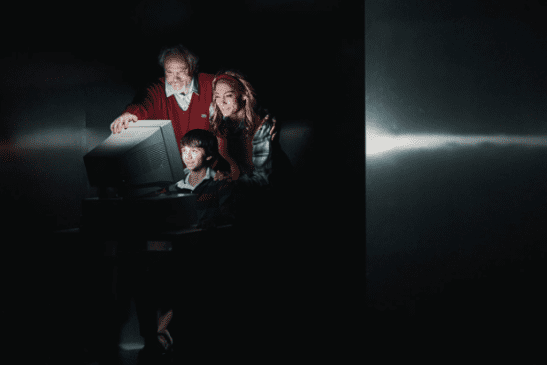Family of three hovering over a lit-up computer screen.