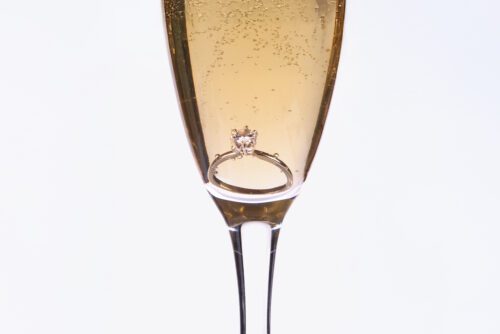 A diamond engagement ring sits at the bottom of a champagne flute filled with sparkling wine.