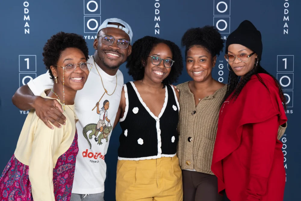 Five people stand together smiling in front of a blue Goodman Theatre 100 Years step-and-repeat backdrop.