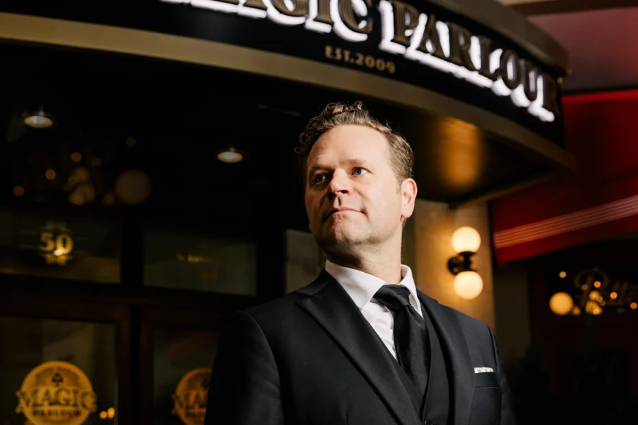 A man in a suit stands outside a building with a sign reading "MAGIC PARLOR" above the entrance.