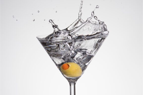 A splash of liquid in a martini glass with a single olive at the bottom.