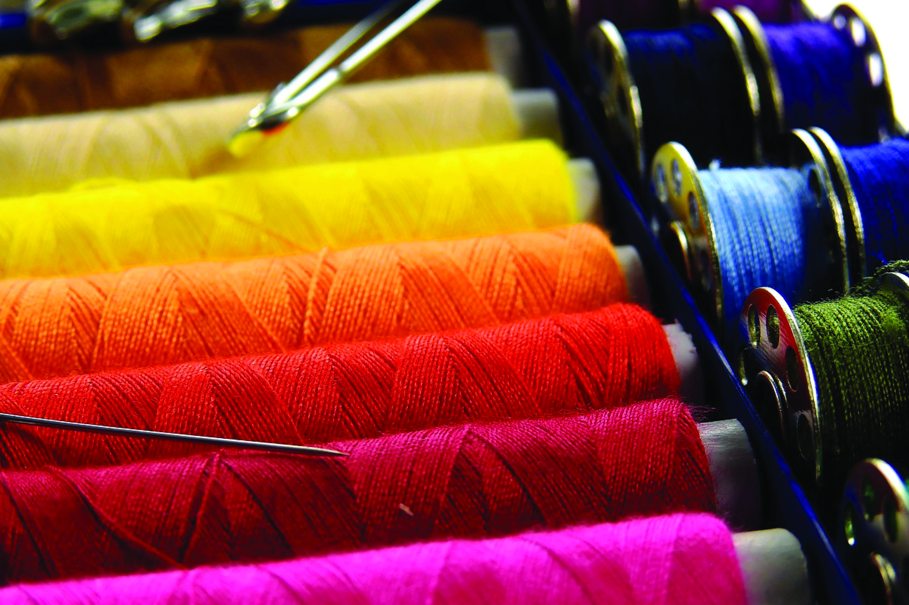 Spools of sewing thread in various colors are arranged in a box with needles and metal bobbins nearby.
