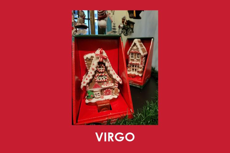 A gingerbread house ornament in a red box is displayed upright on a grassy surface, with another similar ornament in the background. The word "VIRGO" appears at the bottom.