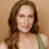 A woman with long wavy blonde hair and blue eyes, wearing a green tank top, poses in front of a beige background.