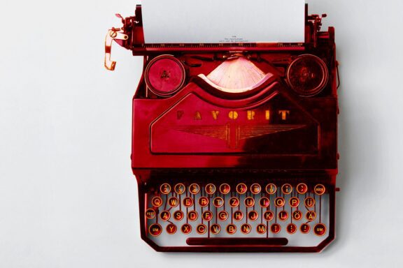 A red vintage typewriter with a sheet of white paper inserted, viewed from above on a white background.