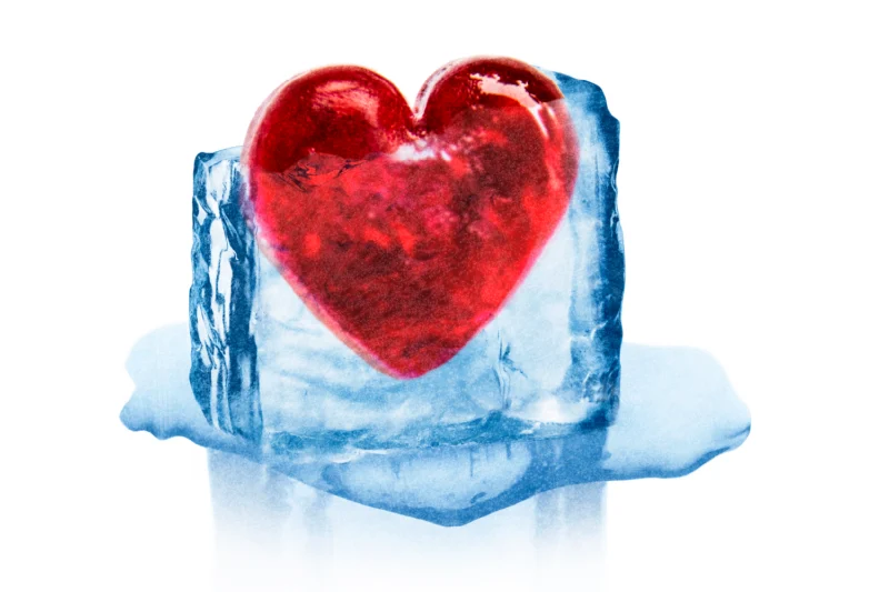 A red heart encased in a melting block of blue ice on a white background.