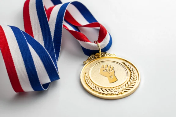 Gold medal with a red, white, and blue ribbon, featuring a raised fist symbol and laurel wreath design on a white background.