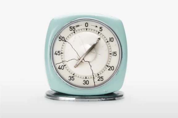 A vintage kitchen timer with cracked glass sits on a white surface, showing approximately 14 minutes.