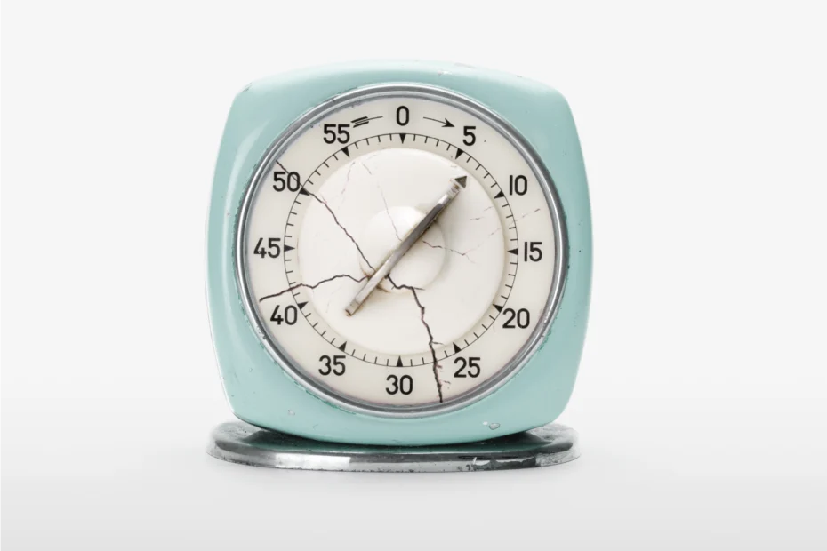 A vintage kitchen timer with cracked glass sits on a white surface, showing approximately 14 minutes.