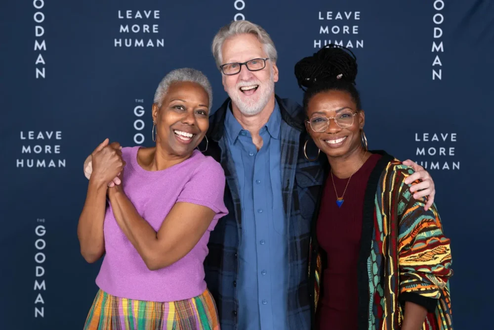 Three people smiling and posing in front of a blue backdrop featuring the text “The Goodman” and “Leave More Human.”