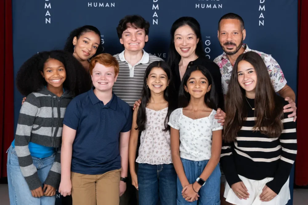 A group of nine people posing for a photo in front of a blue backdrop with “THE HUMAN” text.
