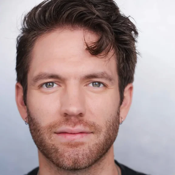 A man with short brown hair and a trimmed beard looks directly at the camera against a plain light background.