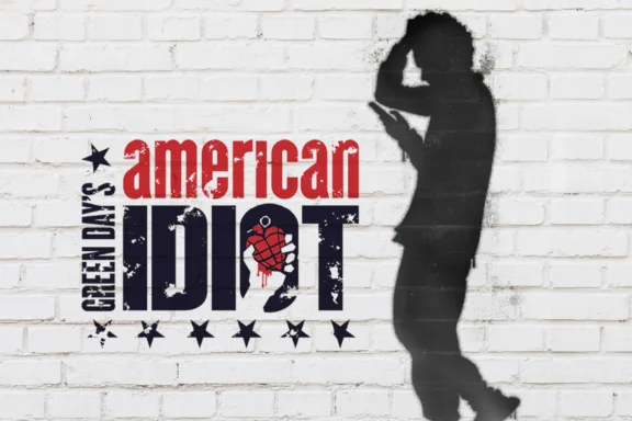 A white brick wall with the text "Green Day's American Idiot" and a silhouette of a person holding their head in distress.