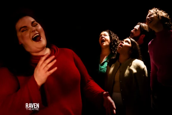 Five people stand dramatically in a dark space, with one person in the foreground singing passionately. The Raven Theatre logo appears in the corner.