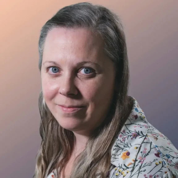 Woman with long, light brown hair and blue eyes wearing a floral shirt, looking at the camera, against a gradient background.