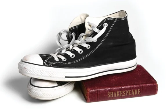 Black high-top sneaker resting on a small, red book titled “Shakespeare.”