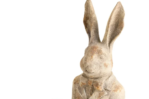 A weathered, textured rabbit figurine wearing a bowtie and jacket.