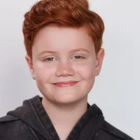 A headshot of a young person with red hair and freckles smiling at the camera.