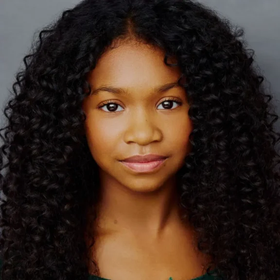 Headshot of a young person with long, curly dark hair looking directly at the camera.